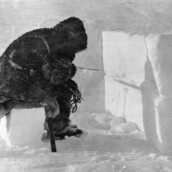 Black and white photo of a person sitting in front of blocks of ice