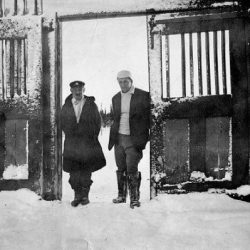 Black and white photo of two men standing in front of a large open doorway