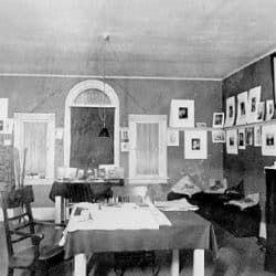 Black and white photo of a room with many photographs scattered across the 3 walls