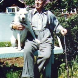 Colour photograph of a man sitting with a dog next to him on a bench