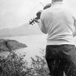 Black and white photo of a man playing a violin, looking down at a lake