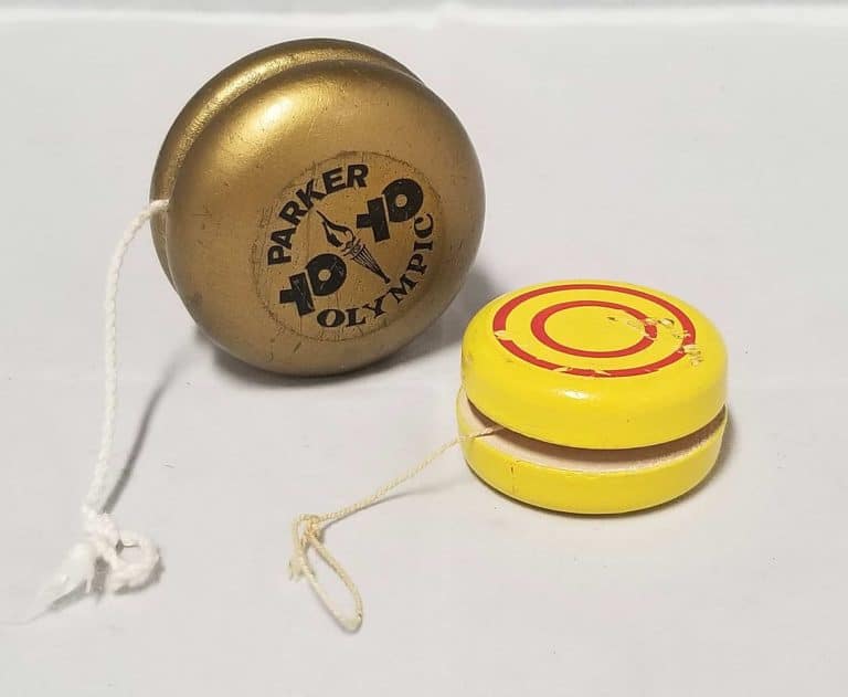 Two yo-yos. One gold coloured with Parker Yo Yo Olympic written on it. The other is yellow with 2 red circles painted on the side.