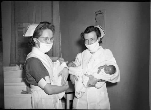 Two nurses in masks holding newborn triplets