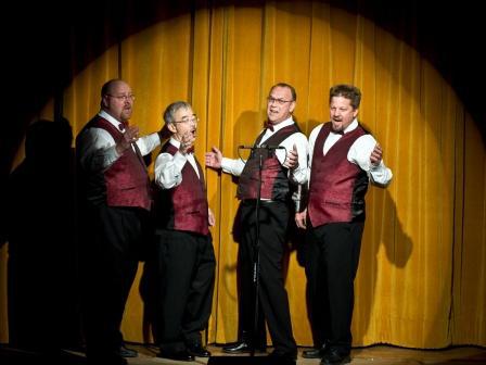 Four men singing on a stage.