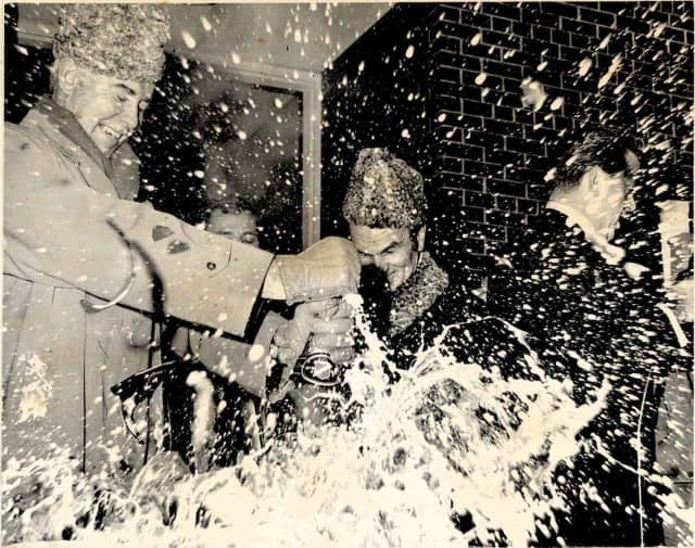 Old photo of men celebrating and opening a bottle of champagne.