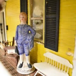 Figurine standing on the porch area near a white bench.