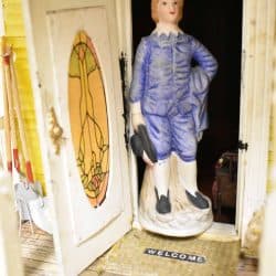Figurine in blue clothes standing in front of the open front door.