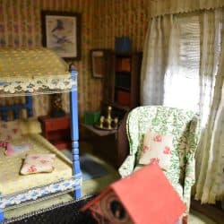 Girls bedroom with a canopy bed, high back chair, and a the top of a doll house.