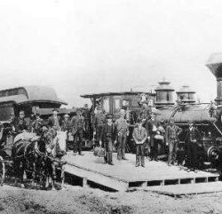 First Locomotive - Old black and white photo with people and horses standing in front of a train engine.