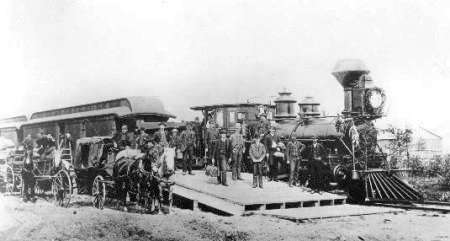 First Locomotive - Old black and white photo with people and horses standing in front of a train engine.
