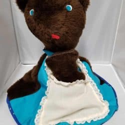 a brown bear with blue eyes and a blue and white apron on and inside the apron is a little brown bear