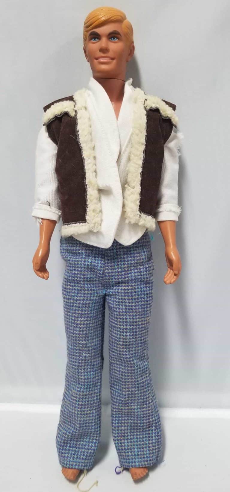 Ken doll wearing a brown vest over a white long sleeve shirt and blue houndstooth pants.