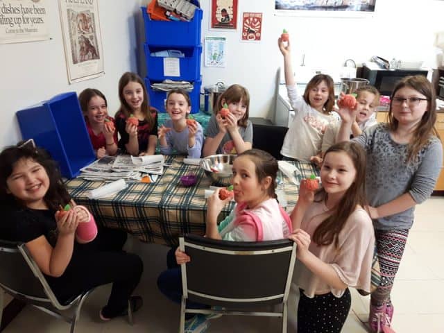 Young girls around a table at a birthday party with peach craft in their hands