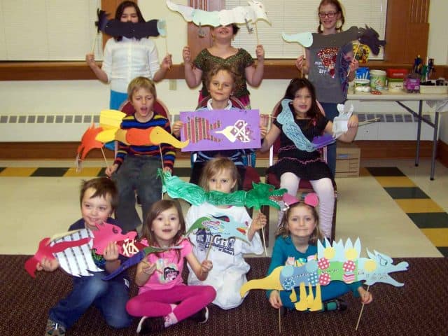 Children holding up paper dragons made during Summer Camp.