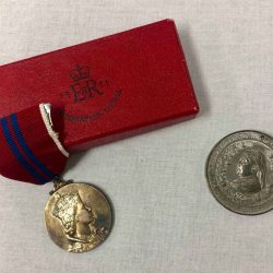 A medal with a drawing of the queen on it. Next to it is a coin with the Queen depicted on it