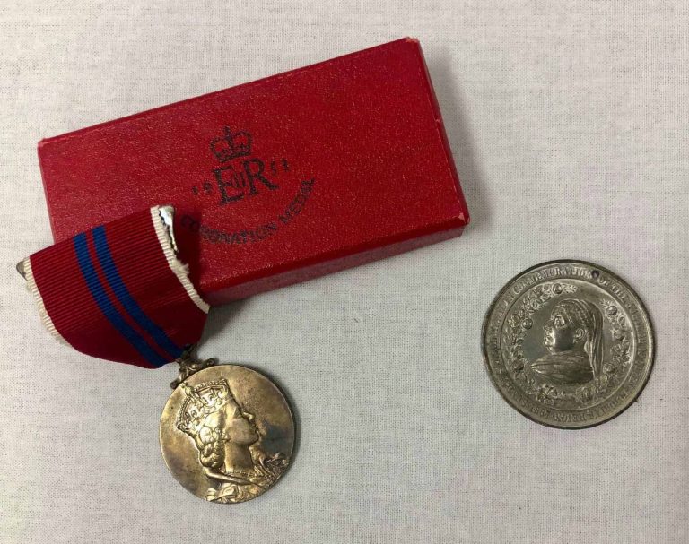 A medal with a drawing of the queen on it. Next to it is a coin with the Queen depicted on it