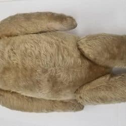 Stuffed teddy bear with hinged moved arms, legs, and head, laying down.