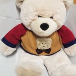 White teddy bear wearing a knit gold, red, and blue sweater with a bear patch on the front.